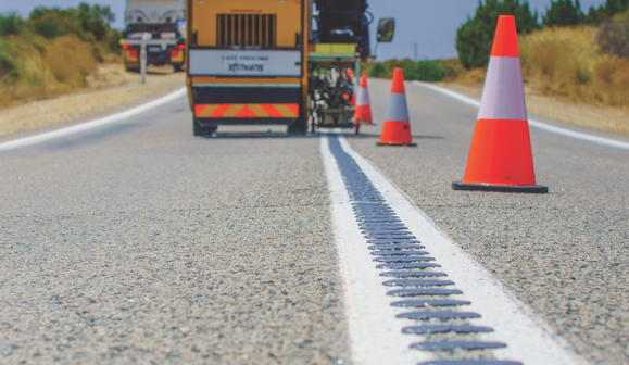 Close up of bitumen road with machinery in background