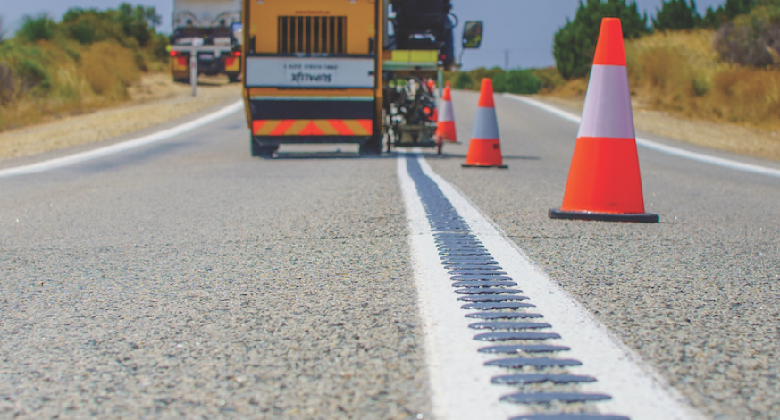 Close up of bitumen road with machinery in background