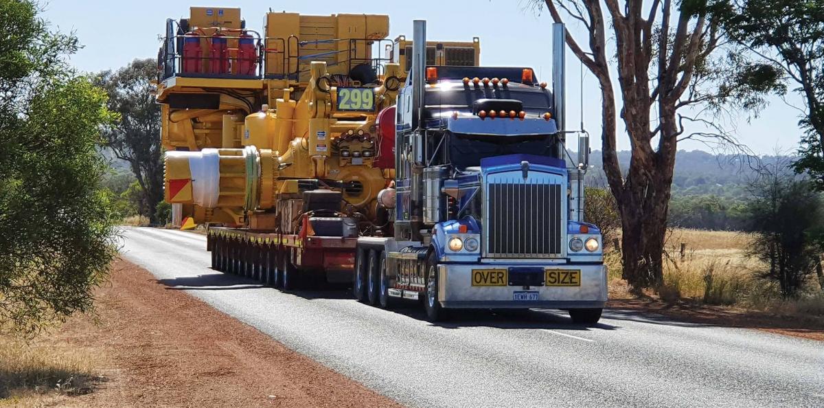 A front view of large truck with an even larger piece of mining equipment on its trailer