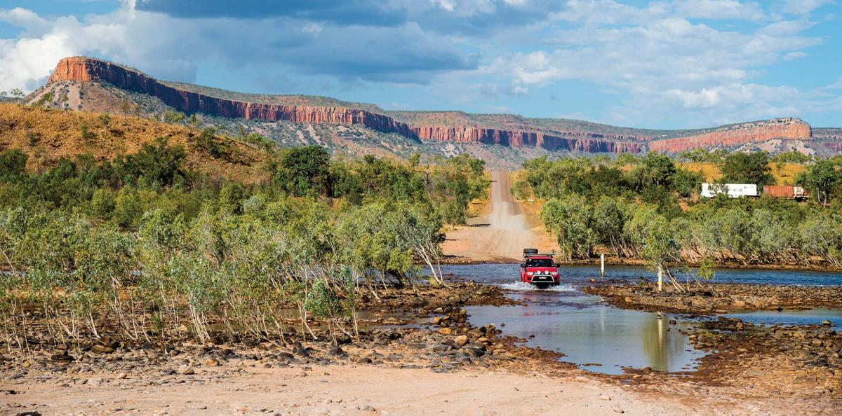 A wide angle landscape shot of 4wd vehicle crossing some water with hills and trees in the background