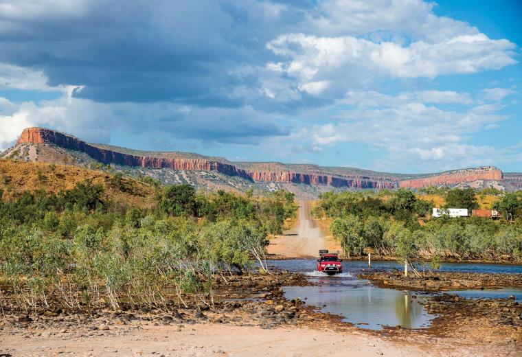 A wide angle landscape shot of 4wd vehicle crossing some water with hills and trees in the background