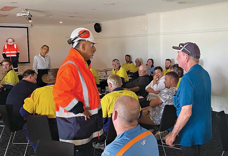 A group of workers in an office. Two are standing  and enacting a scene whilst the others look on.