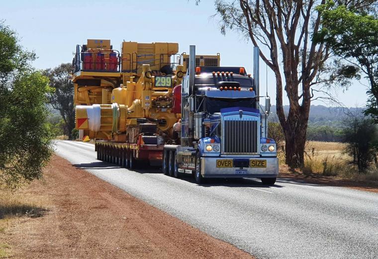 A front view of large truck with an even larger piece of mining equipment on its trailer